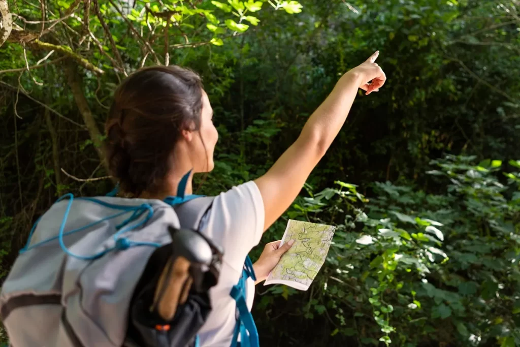  Mulher aventureira segurando um mapa e apontando para a floresta enquanto explora uma trilha ecológica.