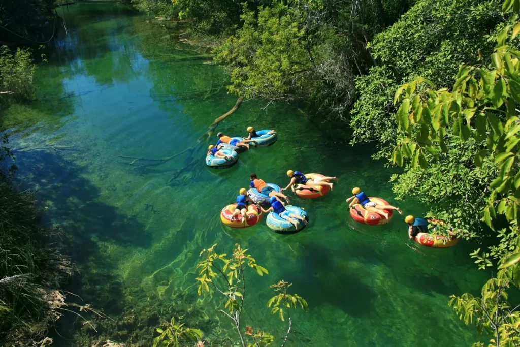 Grupo de aventureiros praticando boia cross em um rio de águas cristalinas, rodeado por vegetação densa, usando capacetes e coletes salva-vidas.