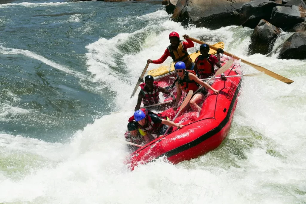 Grupo de aventureiros praticando rafting em um bote inflável vermelho, enfrentando corredeiras intensas em um rio cercado por pedras e vegetação em Bonito.