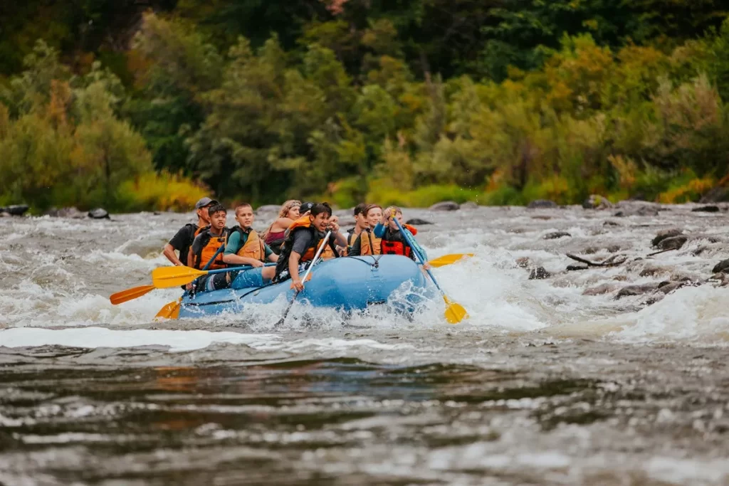 Grupo de aventureiros praticando rafting em um bote azul, descendo um rio com corredeiras cercado por vegetação densa em Bonito.