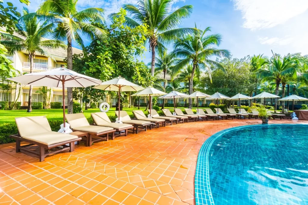 Piscina de resort com espreguiçadeiras acolchoadas, guarda-sóis e área verde tropical ao redor, criando um ambiente perfeito para descanso e lazer.