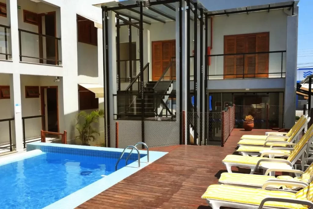 Área externa de hotel econômico em Bonito MS, com piscina azul, espreguiçadeiras amarelas e estrutura moderna ao fundo