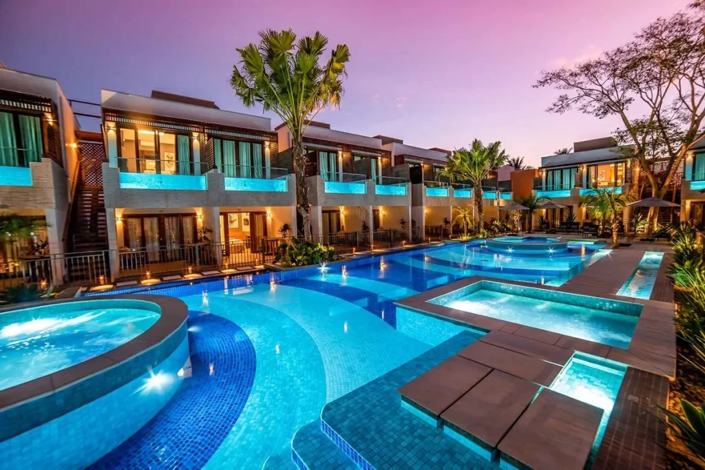 Vista noturna de resort de luxo em Bonito, com piscina iluminada, banheiras de hidromassagem e suítes com varanda decorada.