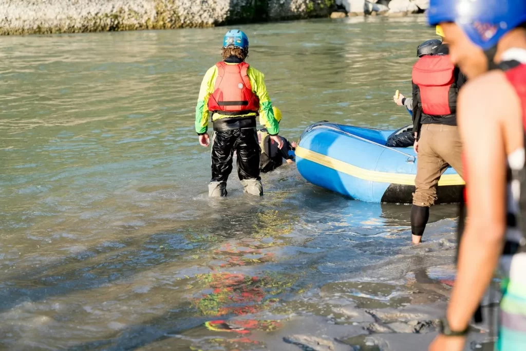 Grupo de pessoas com coletes salva-vidas e capacetes ao lado de bote inflável em rio raso
