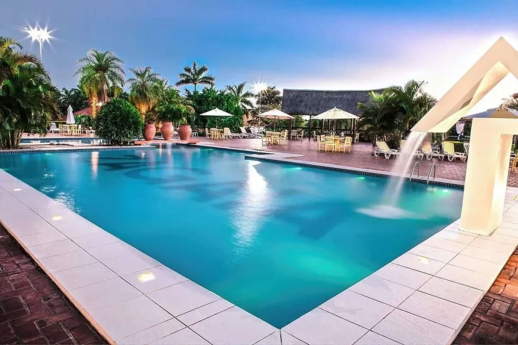 Vista aérea de resort com parque aquático infantil, piscinas, quadra de esportes e amplas áreas verdes cercadas por palmeiras