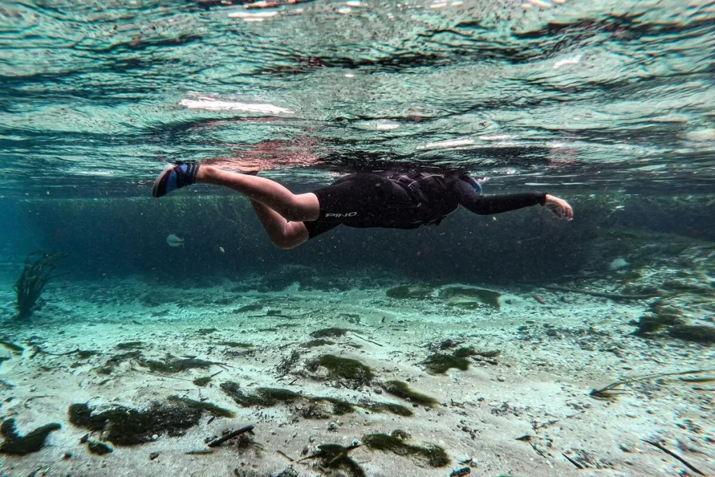 Pessoa praticando flutuação em rio cristalino com equipamentos de snorkel.