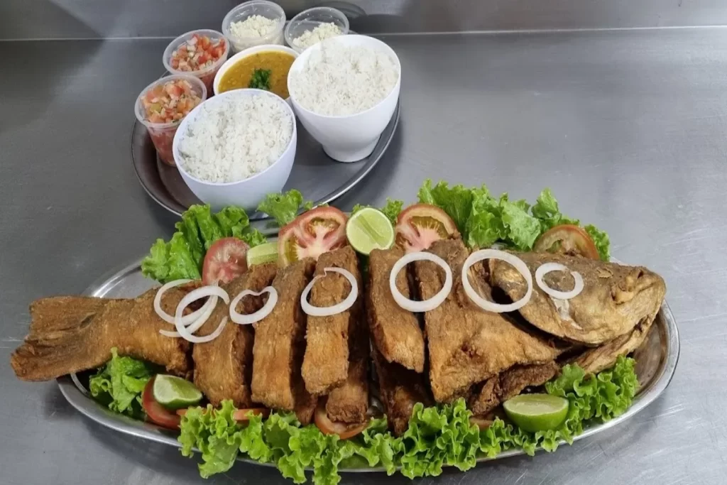 Prato de tucunaré frito servido com arroz, farofa, vinagrete, feijão e salada de folhas, tomate e cebola