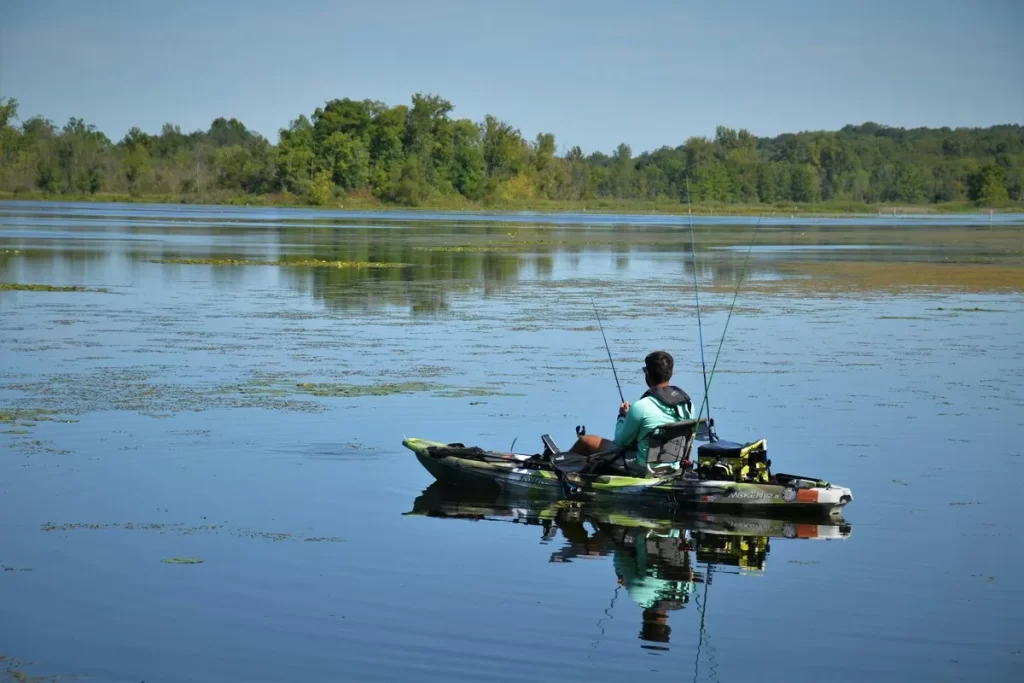 Homem pescando em caiaque em lago calmo rodeado por vegetação, atividade típica no Pantanal brasileiro.