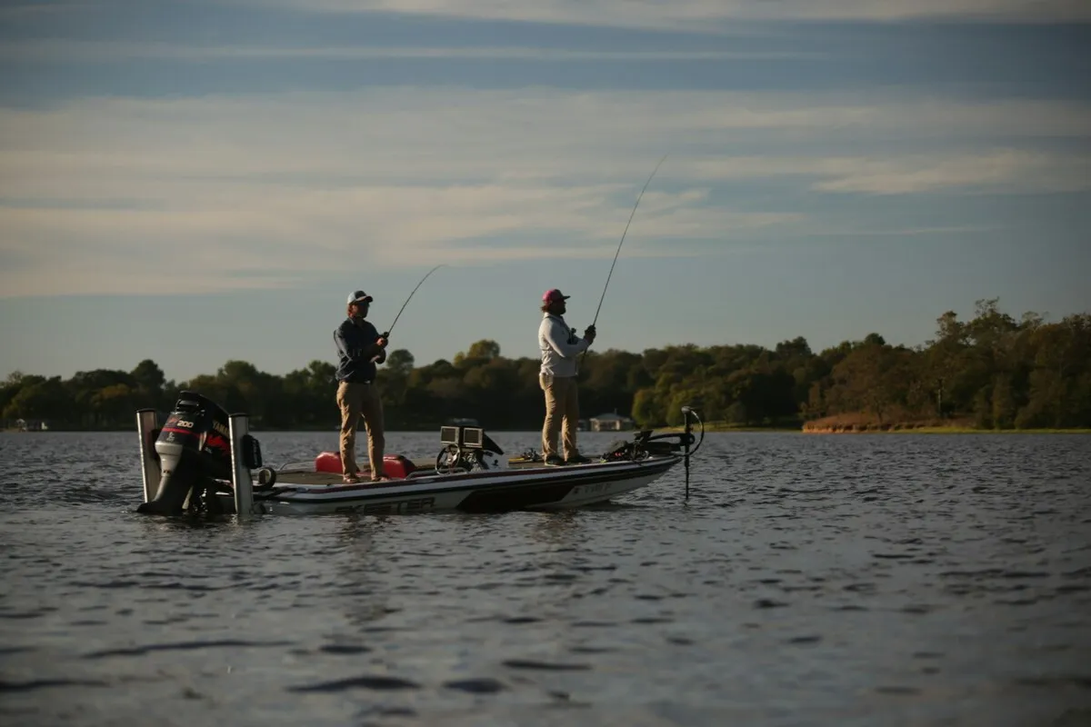 Dois pescadores em barco motorizado pescando em lago cercado por mata.