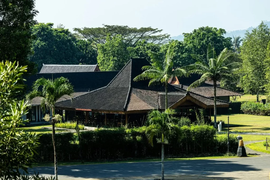 Edifício com telhado tradicional e palmeiras em meio a paisagem verde, perfeito para hospedagem em Bonito MS.