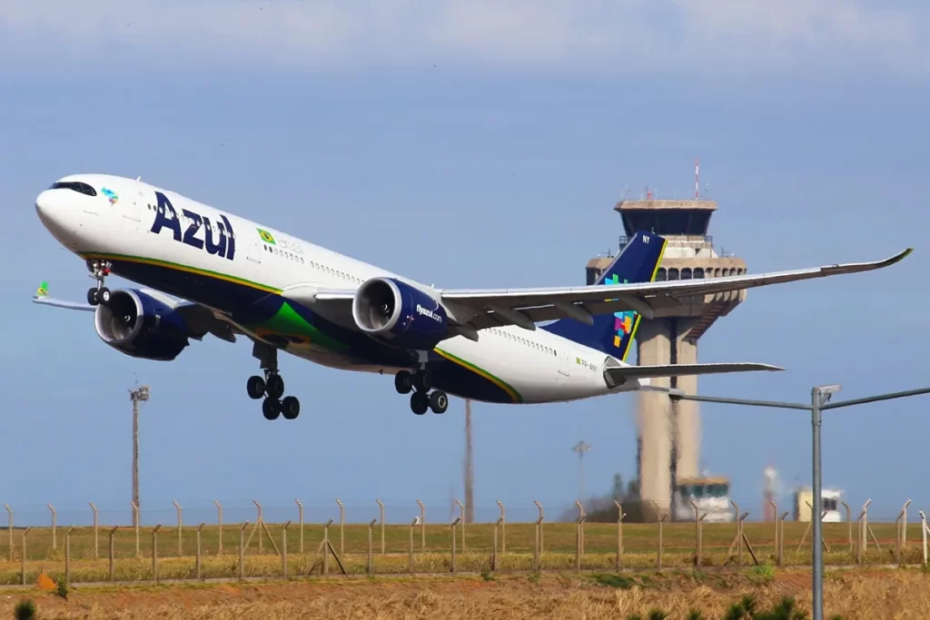 Avião Airbus A330 da Azul Linhas Aéreas decolando em pista, com torre de controle ao fundo e céu claro