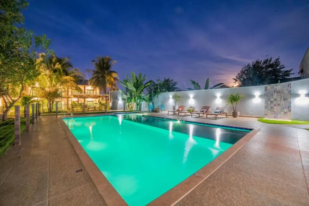 Vista noturna da área de lazer da Pousada Girassol Bonito MS, com a piscina iluminada e espreguiçadeiras.