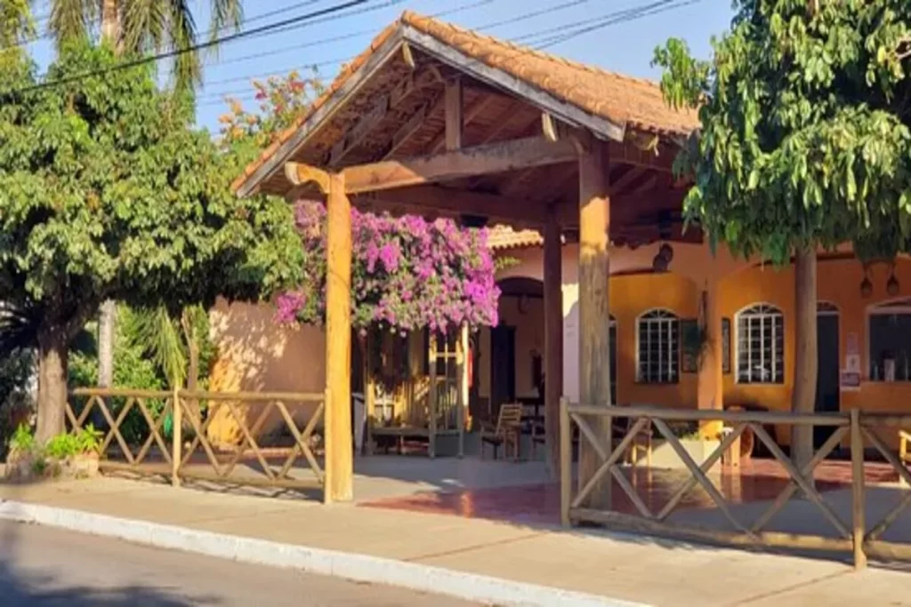 Fachada rústica e charmosa de um hotel no Pantanal, com telhado de telha, varanda de madeira e uma cerca de madeira.