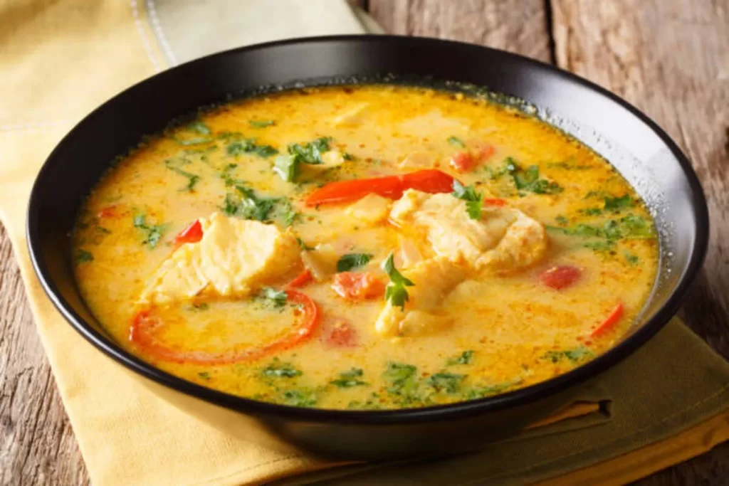 Uma tigela de moqueca de peixe sobre um pano de prato amarelo. A imagem destaca a aparência apetitosa do prato, com as cores vibrantes dos vegetais e a consistência cremosa do caldo, ingredientes que o tornam uma opção nutritiva e saborosa.