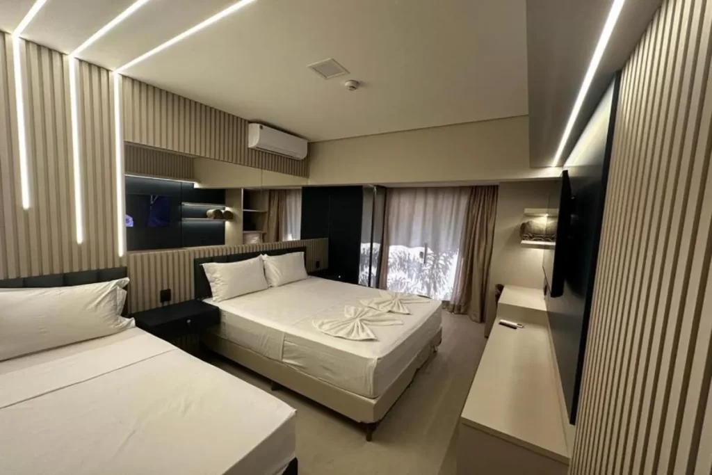 Quarto moderno da Pousada Villas Bonito com duas camas de casal, iluminação de LED embutida e decoração minimalista em tons neutros.