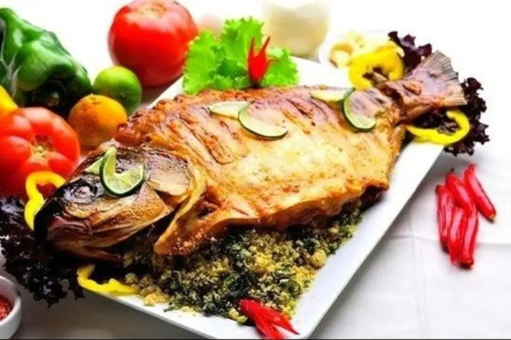 Um pacu assado inteiro, com a pele dourada, servido em um prato branco sobre uma cama de farofa, decorado com rodelas de limão e um arranjo colorido de tomates, pimentões e pimentas.