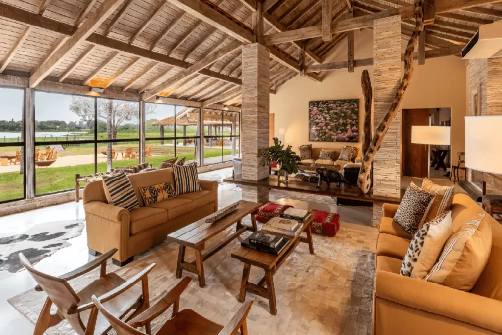 Interior luxuoso de lounge no Refúgio Ecológico Caiman Pantanal com sofás confortáveis, tapete de couro e vista panorâmica para a natureza.